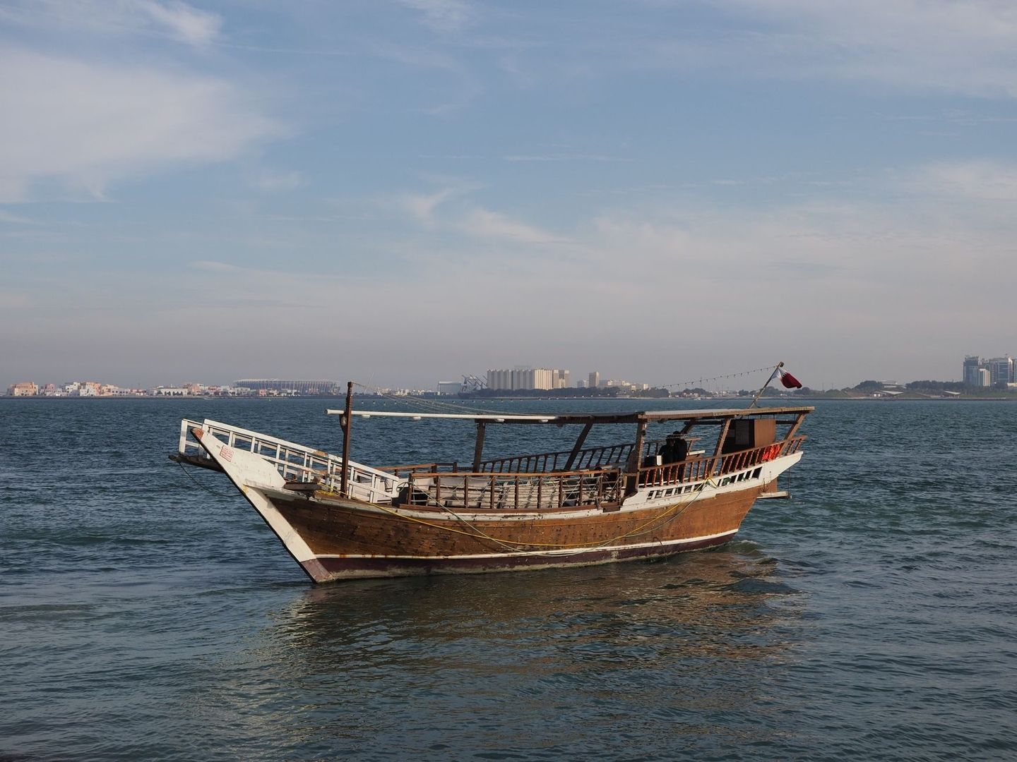 Traditionele houten dhow op kalm water voor een kuststad