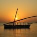 Traditionele houten dhow bij zonsondergang op kalm zeewater