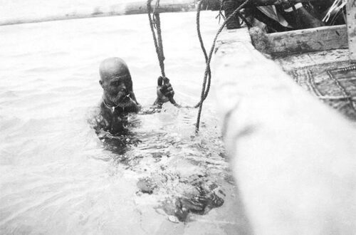 Zwart-witfoto van een man in zee naast een houten boot