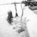 Zwart-witfoto van een man in zee naast een houten boot