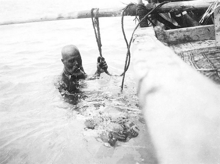 Zwart-witfoto van een man in zee naast een houten boot